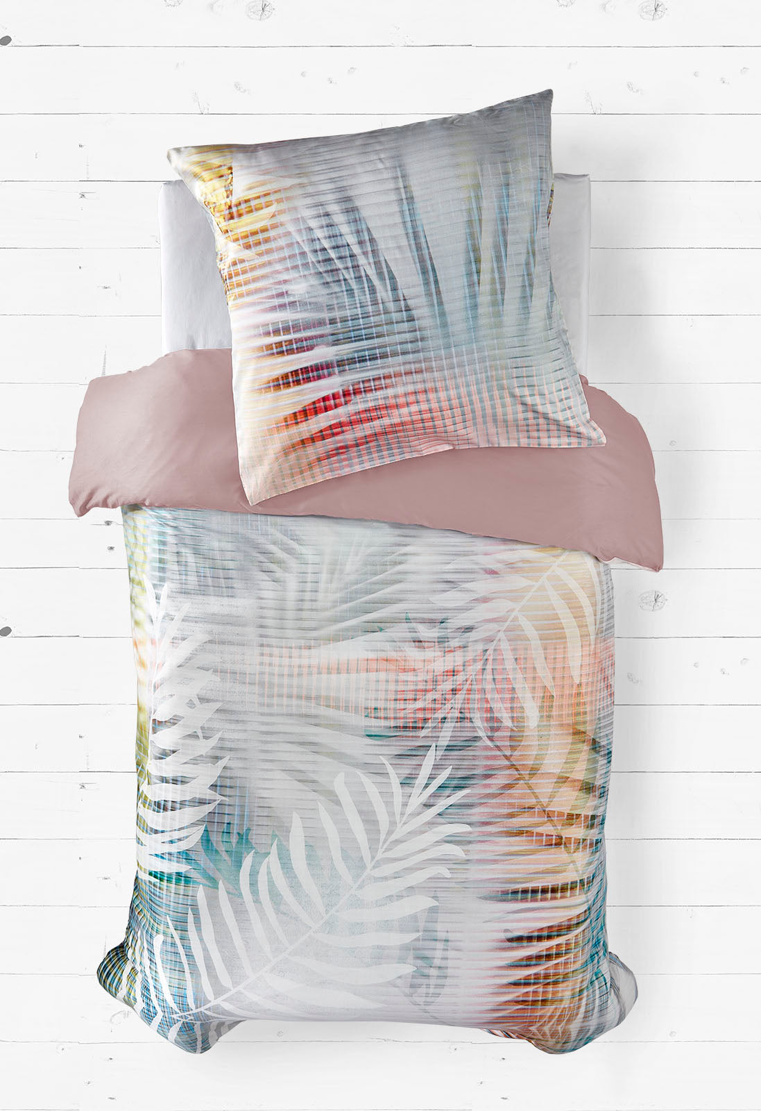 Dieses Bild zeigt ein modernes Bettwäscheset mit einem stilvollen, tropischen Blattmuster. Die sanften, pastellfarbenen Töne und die dezenten Rasterlinien verleihen der Bettwäsche eine elegante, beruhigende Ästhetik. Der Hintergrund aus weißen Holzdielen betont das frische, luftige Design.