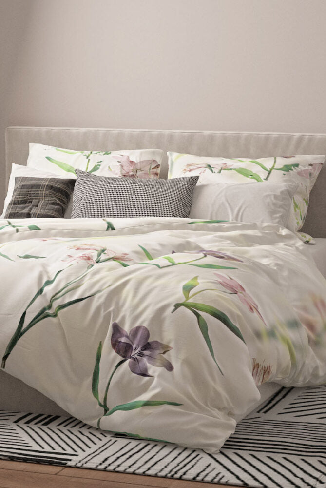 Bettwäsche-Set mit floralen Motiven auf hellem Hintergrund. Das Design zeigt violette, rosa und lachsfarbene Blumen mit grünen Stängeln und Blättern. Die Unterseite des Bettbezugs und das Laken sind in einem sanften Grünton gehalten.