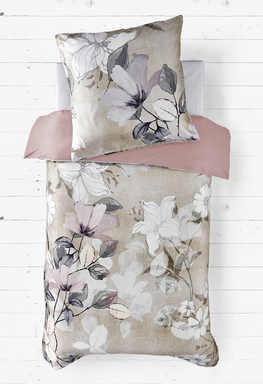 Das Bild zeigt ein Bettwäsche-Set mit einem floralen Muster. Die Bettdecke und das Kissen sind mit großen Blumen in sanften Beige-, Grau- und Lila-Tönen verziert. Der Hintergrund hat eine leicht strukturierte Optik, die an Leinen erinnert. Das Spannbettlaken ist in einem einfarbigen, gedeckten Rosaton gehalten. Die Gesamtästhetik ist elegant, dezent und wirkt beruhigend.